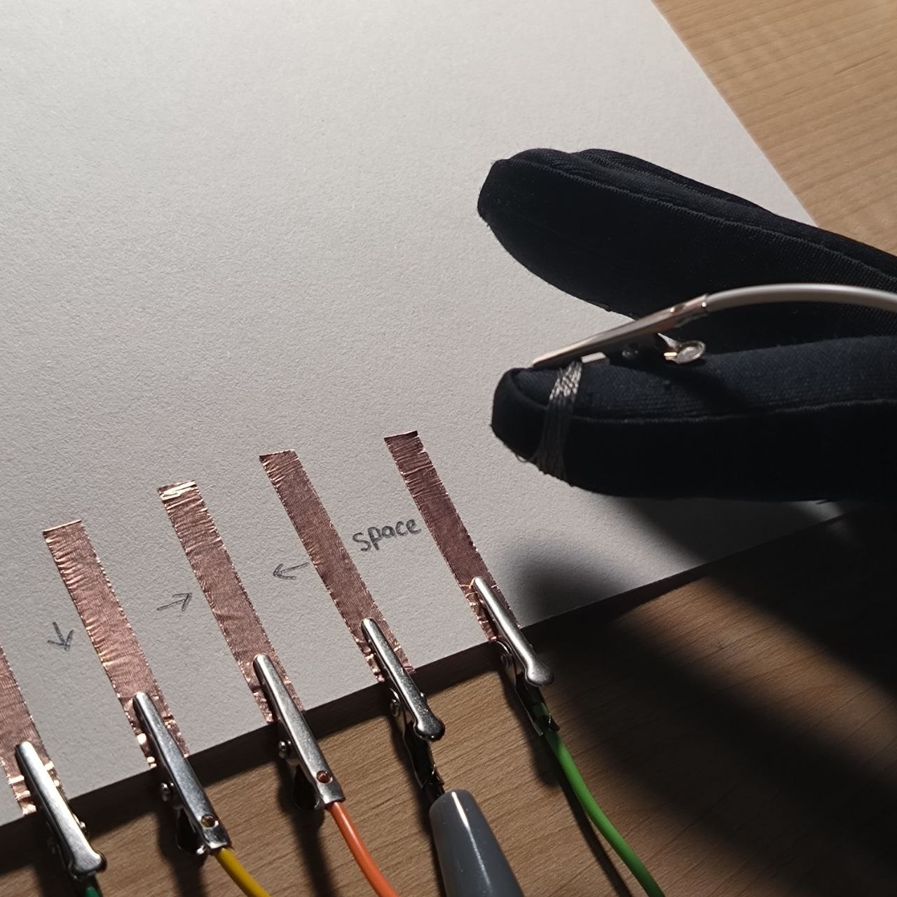 The modified glove touches the space copper strip. Because the glove is wired for conductivity, this contact sends an input signal—demonstrating that the glove-controller is working.